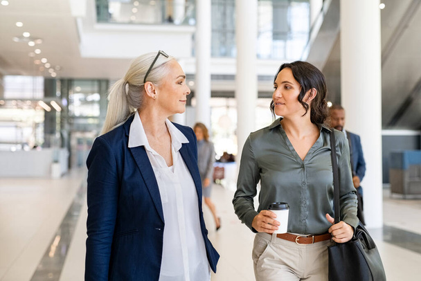 Two business women walking and talking in modern office. Two successful women manager discussing work while entering office building. Successful mature business woman talking with her assistant while going to work. - Foto, Bild