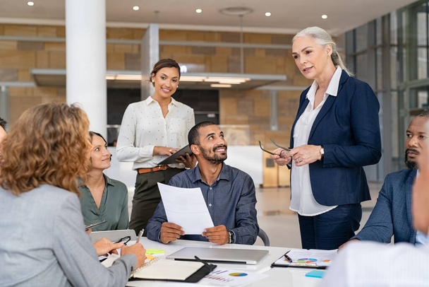 Group of mixed race business people discussing work in conference room. Senior business manager guiding employees in meeting. Group of businessman and businesswoman working together while brainstorming and sharing new ideas and strategy. - Foto, afbeelding
