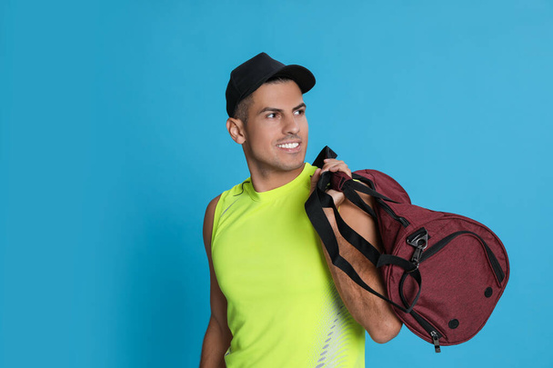 Handsome man with sports bag on light blue background - Foto, imagen