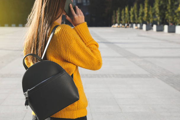 Young woman with stylish black backpack talking on phone outdoors, closeup. Space for text - Fotoğraf, Görsel