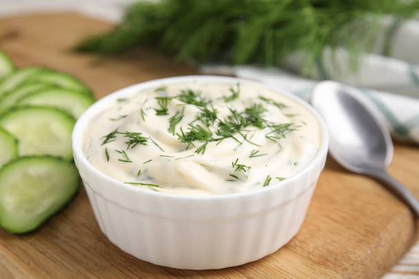Tasty creamy dill sauce in bowl on wooden board, closeup - Photo, image