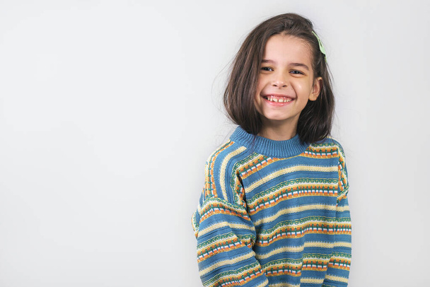 Studio portrait of joyful charming beautiful cute little girl with long smooth straight hair smiling and looking to the camera isolated on white background. Pretty child has positive emotion. - 写真・画像