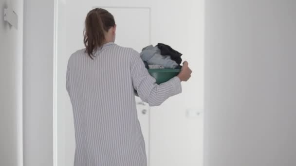 Uitzicht van achteren, een vrouw huisvrouw in een hydraterende masker op haar gezicht draagt een wastafel met vuile was - Video