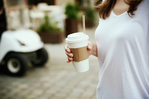 Woman holds paper coffee cup at city street - Фото, зображення