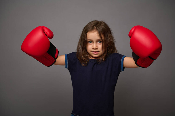 Cute European 4 years old baby girl wearing red boxing gloves poses against gray wall background with copy space for advertisement for Boxing Day - Foto, afbeelding