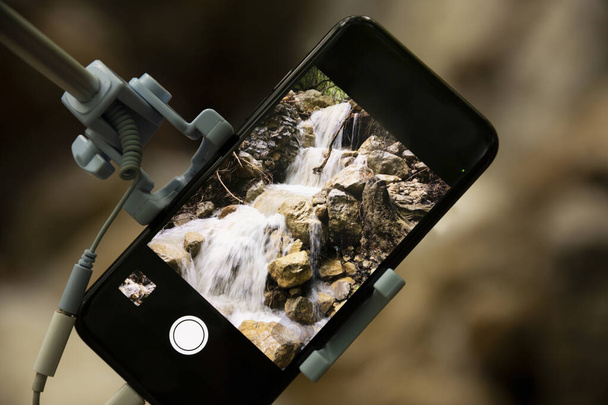 Taking pictures using a smartphone with a selfie stick on a blurred beautiful background. Close-up. - Foto, imagen
