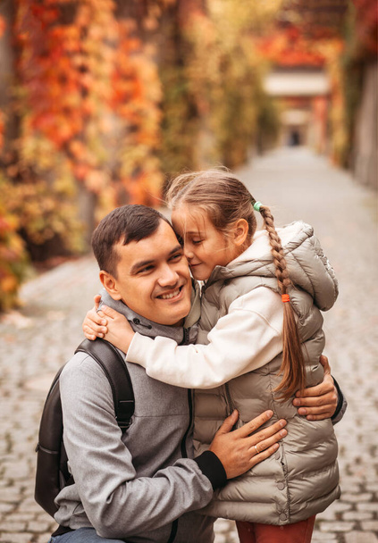 Ο νεαρός χαρούμενος μπαμπάς και η μικρή κόρη αγκαλιάζονται στο πάρκο το φθινόπωρο. Οικογενειακός χρόνος, ομαδικότητα, γονική μέριμνα και χαρούμενη παιδική ηλικία. Σαββατοκύριακο με συναισθήματα. - Φωτογραφία, εικόνα
