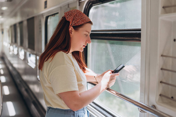 Uma bela mulher hipster com smartphone viajando no trem na Europa. Viagens turísticas, navegar na internet, conceito de compras on-line de produtos. Freelancer vai em viagem - Foto, Imagem