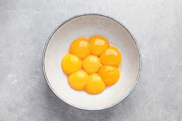 Bowl with raw egg yolks on grey table, top view - Foto, afbeelding