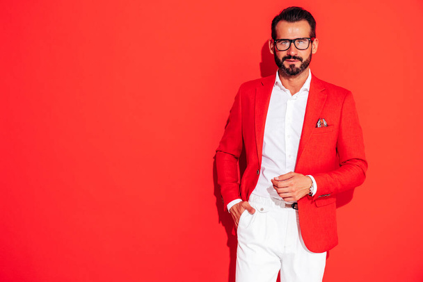 Portrait of handsome confident stylish hipster lambersexual model. Sexy modern man dressed in elegant suit. Fashion male posing in studio near red wall in spectacles - Φωτογραφία, εικόνα