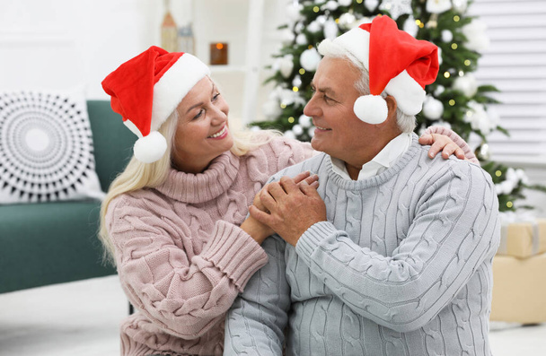 Happy mature couple in Santa hats at home. Christmas celebration - Foto, Imagem
