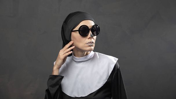 Beautiful woman wearing nun costume and halloween makeup over dark gray background - Photo, Image