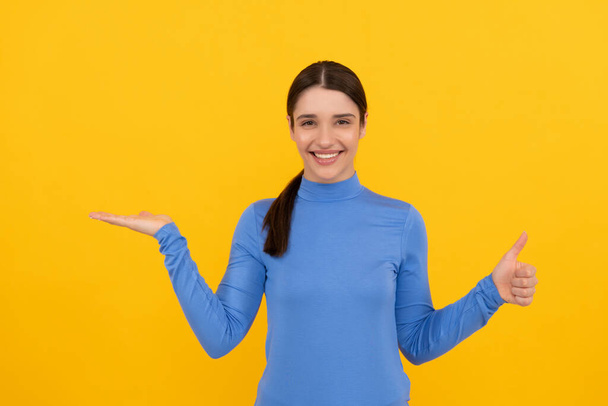 amazed woman portrait pointing fingers on copy space yellow background showing thumb up, emotions - Photo, Image