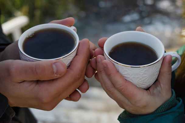 White cups with a hot drink in the hands of man and a woman. Romance and travel concept - Φωτογραφία, εικόνα