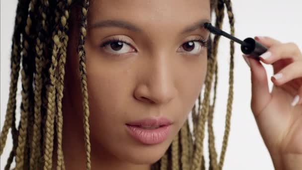 Afrikai-amerikai fiatal nő alkalmazó szempillaspirál a szempillák, fehér háttér - Felvétel, videó
