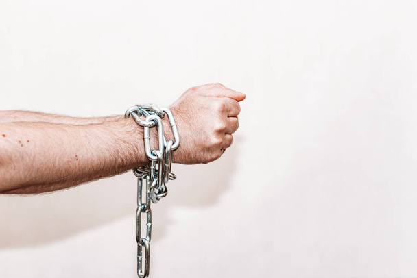 Men's hand in a steel chain.Steel chains in the hands of man on a gray wall background.Toned.Closeup,selective focus.Copy space. - Photo, Image