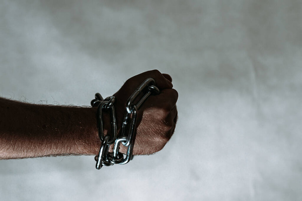 Men's hand in a steel chain.Steel chains in the hands of man on a gray wall background.Toned.Closeup,selective focus.Copy space. - Foto, imagen