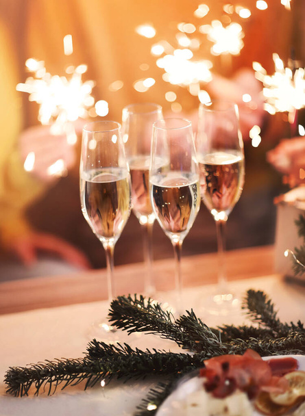 Glasses of champagne on table with blurred background of festive lights and elegant peoples hands holding xmas sparkles, panoramic view of friends celebrate new year eve or birthday with happiness - Photo, Image