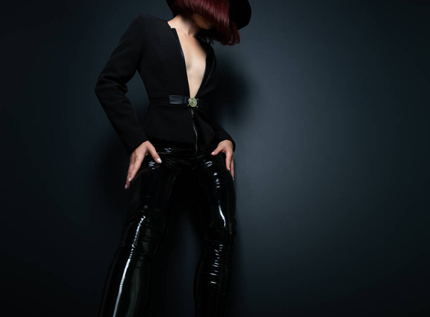 Siyah ceketli, lateks dar pantolonlu ve gri arka planda stüdyoda poz veren güzel moda kadını. - Fotoğraf, Görsel