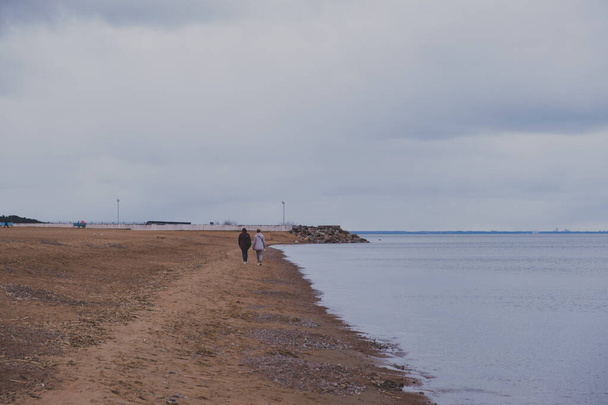 Línea de costa de playa de mar vacía con siluetas de gente. tiempo oscuro sombrío - Foto, Imagen