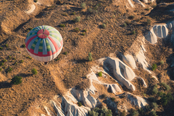 朝の光の中でカッパドキア谷のパノラマの上に青い色と赤い色のパターンを持つ孤独な熱気球のトップビューの閉鎖  - 写真・画像