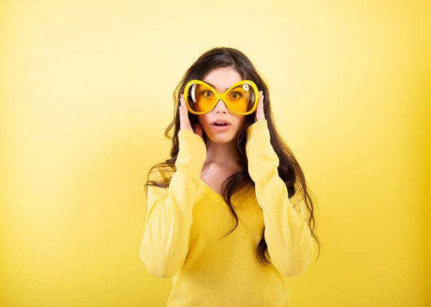 Joyful excited surprised young woman with big funny glasses over yellow background.  - Foto, Bild