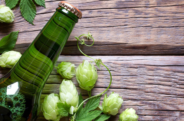 Bottle of beer with hop cones on wooden background - Foto, imagen