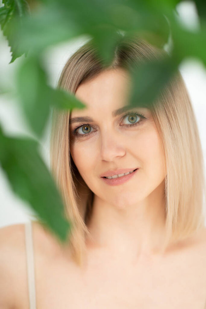 Beautiful calm middle aged woman with green plant, natural light. Anti-aging and beauty treatment.  - Valokuva, kuva