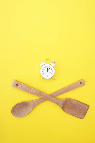 Zestaw bambusowych naczyń i biały zegar vintage na jasnożółtym tle. Koncepcja gotowania. - Zdjęcie, obraz