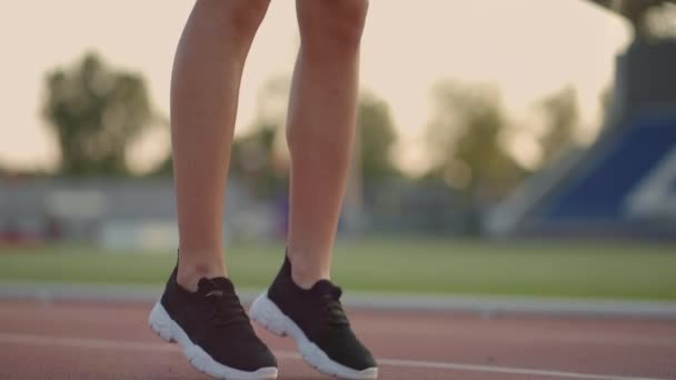 Egy fiatal női sportoló elmélázik, és felkészül egy sprintverseny kezdetére egy napsütéses napon a stadion futópadján. - Felvétel, videó