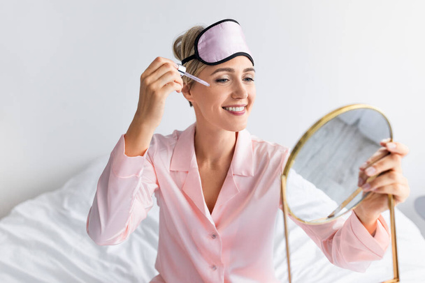 Retrato de mulher sorridente segurando espelho aplicando soro essencial - Foto, Imagem