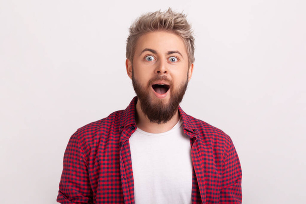 Portrait of extremely surprised caucasian bearded man looking at camera with open mouth and big eyes, happy satisfied with good cashback. Indoor studio shot isolated on gray background - Photo, Image