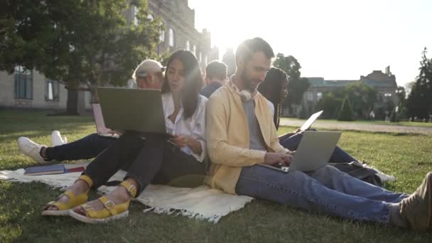 Koledzy z klasy międzynarodowej studiujący na trawniku kampusu - Materiał filmowy, wideo