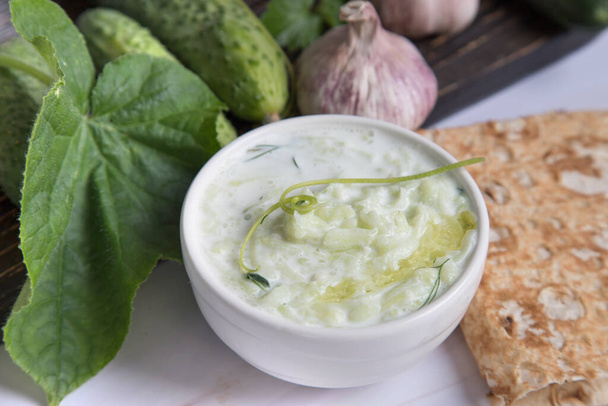 Close-up of tzatziki sauce with pita bread and cucumbers on a wooden board in the background. - Photo, Image