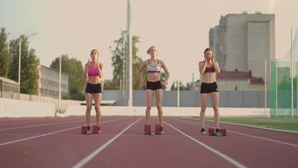 Trois athlètes féminines de piste et d'eau commencent la course au stade dans des coussinets de course à une distance de sprint. Les coureuses de piste et de file courent dans le stade - Séquence, vidéo