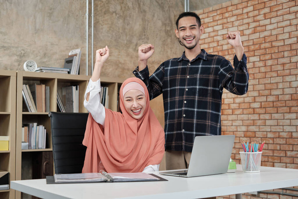 Young startup partners who are Islamic people stand, raise their hands to congratulate the success of small office e-commerce businesses. Two couple colleagues smile and are happy working. - Photo, Image