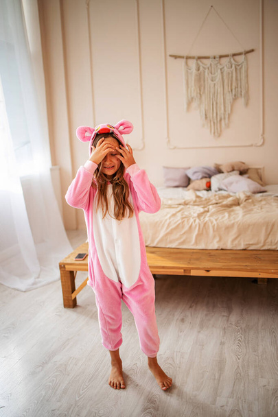 девочка одета в теплые смешные пижамы, играет в бетонной скандинавской внутренней спальне, комфортная сцена. - Фото, изображение