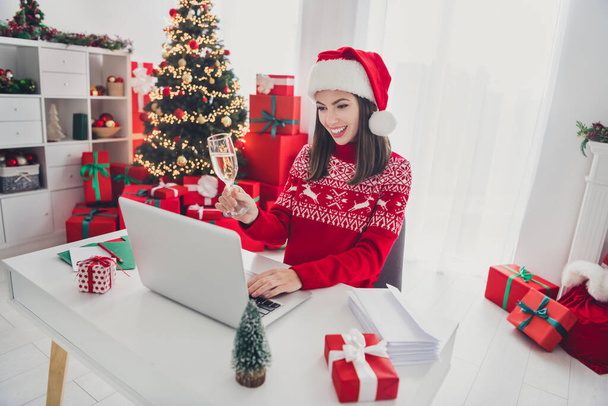 Photo of funny freelancer lady sit workplace make champagne toast wear santa hat sweater in decorated x-mas home indoors - Fotó, kép