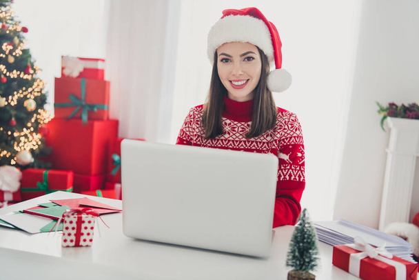 Photo of remote programmer lady sit table typing netbook email wear santa hat pullover in decorated x-mas home indoors - Фото, зображення