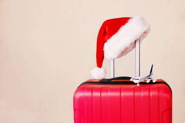 Egy piros bőrönd, egy Mikulás kalap és egy kis repülő. A koncepció az utazás karácsonyra és újévre.  - Fotó, kép