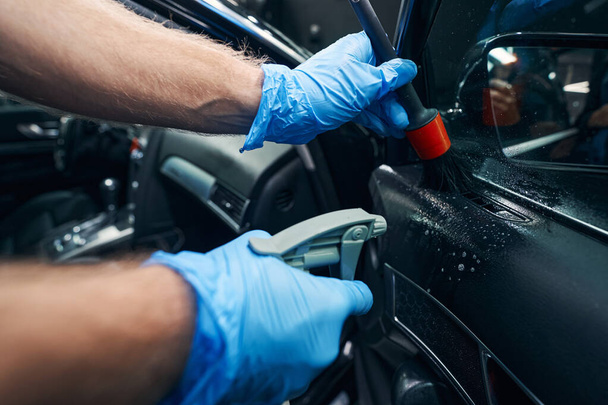 Auto technician using trigger bottle and brush during car cleaning - Foto, Bild