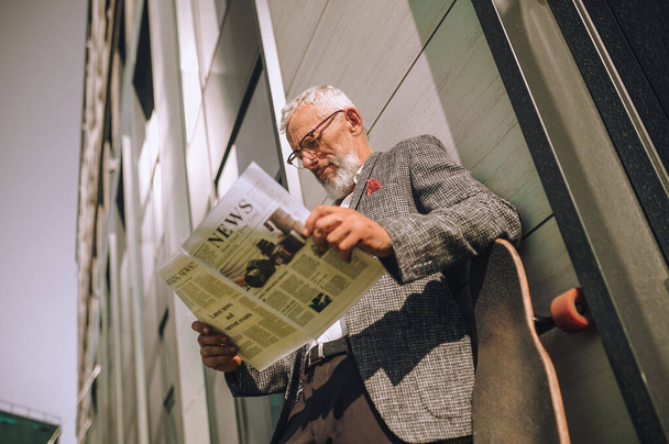 A gray-haired businessman reading a newspaper and looking concentrated - Фото, зображення