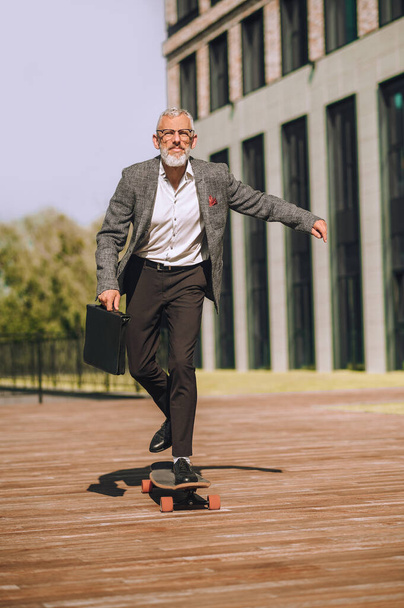 Un uomo d'affari che guida uno skateboard di fronte all'edificio degli uffici - Foto, immagini