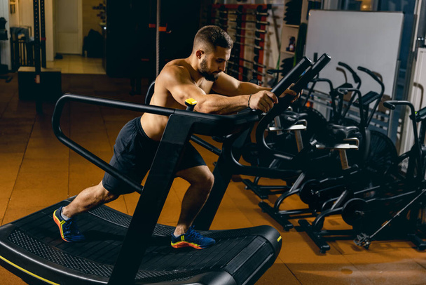 Retrato recortado del hombre deportivo haciendo ejercicios en una cinta de correr, yendo cuesta arriba. Entrenamiento de gimnasia - Foto, Imagen