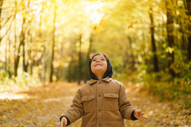 Niño pequeño y feliz niño riendo y jugando en el día de otoño. Niño jugar con hojas - Foto, imagen