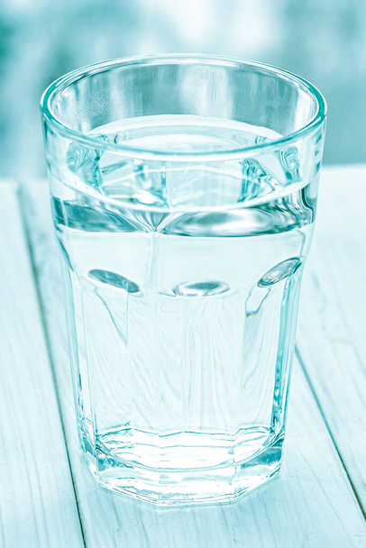 Ένα ποτήρι με καθαρό νερό. Ποτήρι νερού με μισογεμάτο νερό στο τραπέζι, έννοια της θετικής και αρνητικής σκέψης - Φωτογραφία, εικόνα