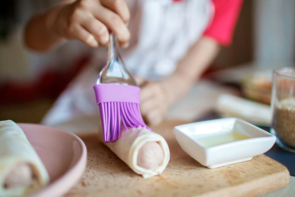 Dziewczyna gotowanie kiełbasa toczona w ciasta phyllo na śniadanie, mały kucharz cieszy smaczne przekąski - Zdjęcie, obraz