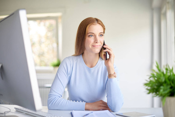 Smiling young businesswoman having a call while sitting at desk and at the office.  - Φωτογραφία, εικόνα