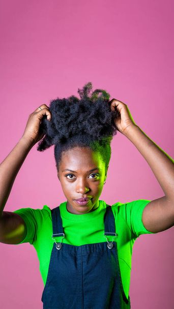 Studio πορτρέτο νεαρή μαύρη γυναίκα ψάχνει φωτογραφική μηχανή θετική και χαμογελώντας αγγίζοντας σγουρά μαλλιά απομονωμένη διαφήμιση αντίγραφο χώρο φόντο - Φωτογραφία, εικόνα