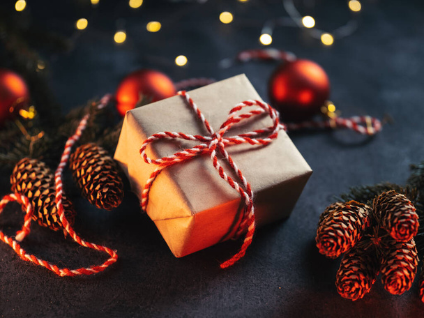 Подарок на Рождество упакован собственными руками и связан красной и белой нитью. Темный вечерний фон - Фото, изображение